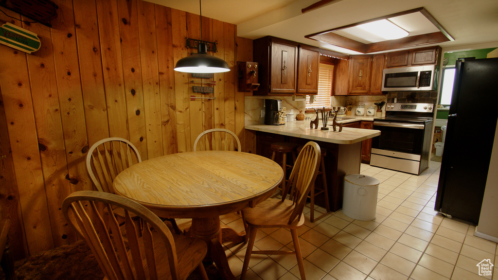 Kitchen featuring appliances with stainless steel finishes, light countertops, a peninsula, light tile patterned floors, and wood walls