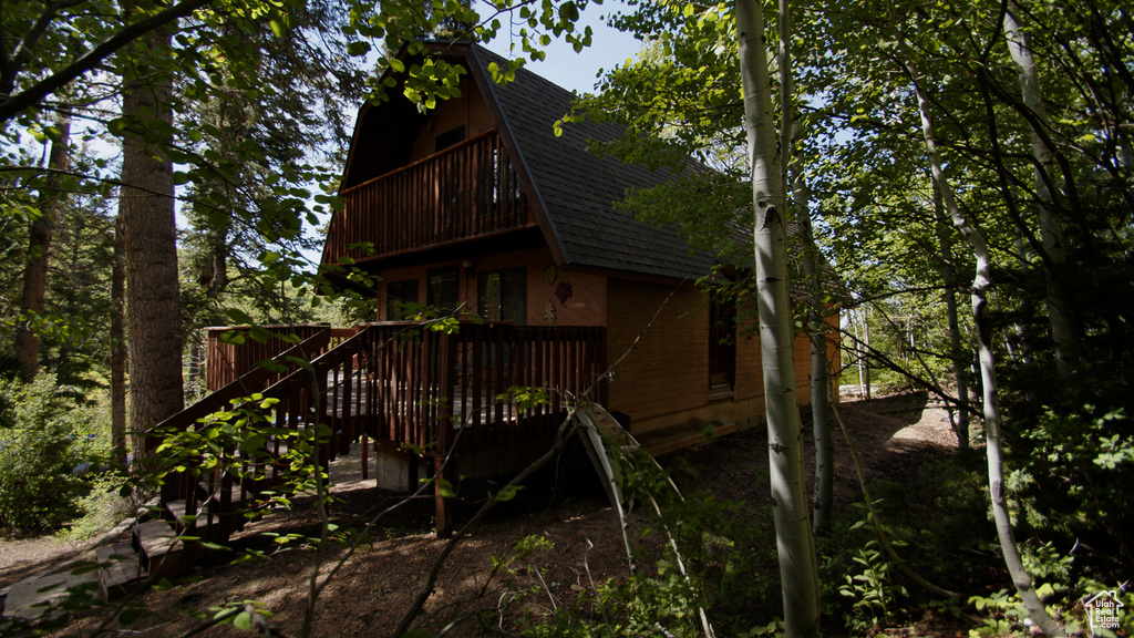Back of property with a shingled roof, a wooden deck, and stairway