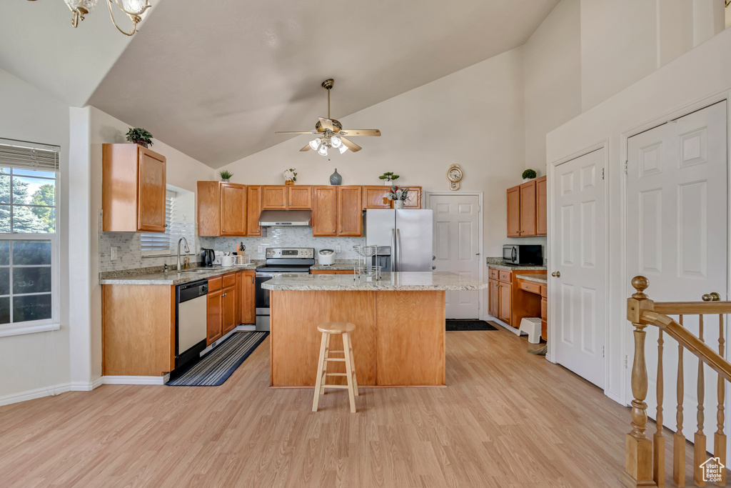 Kitchen with appliances with stainless steel finishes, under cabinet range hood, light wood-style flooring, backsplash, and high vaulted ceiling