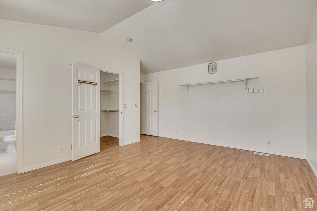 Unfurnished bedroom with light wood finished floors, lofted ceiling, baseboards, a spacious closet, and connected bathroom