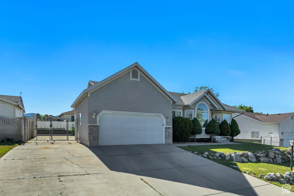 Ranch-style house featuring concrete driveway, an attached garage, a gate, and stucco siding