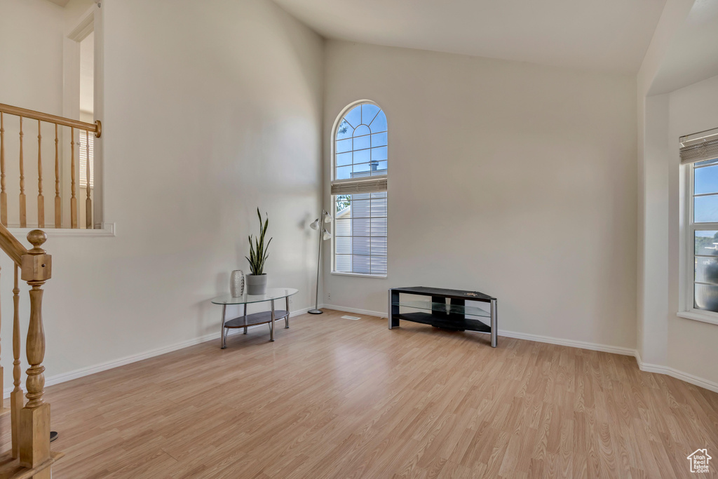 Empty room featuring light wood-style flooring, plenty of natural light, baseboards, and a high ceiling