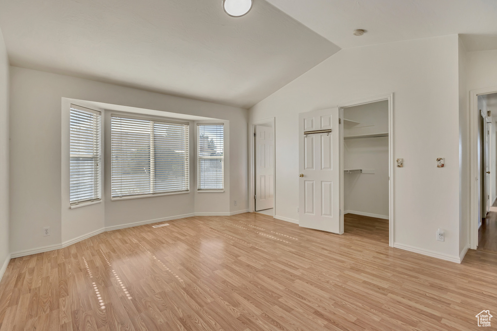Unfurnished bedroom with vaulted ceiling, light wood-type flooring, a walk in closet, baseboards, and a closet