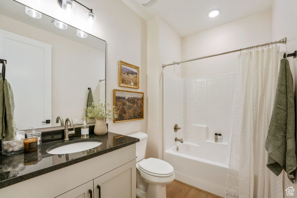 Bathroom with vanity, shower / bathtub combination with curtain, toilet, and wood finished floors