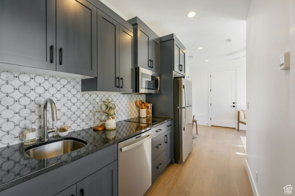 Kitchen featuring appliances with stainless steel finishes, a sink, light wood-style flooring, dark stone countertops, and decorative backsplash