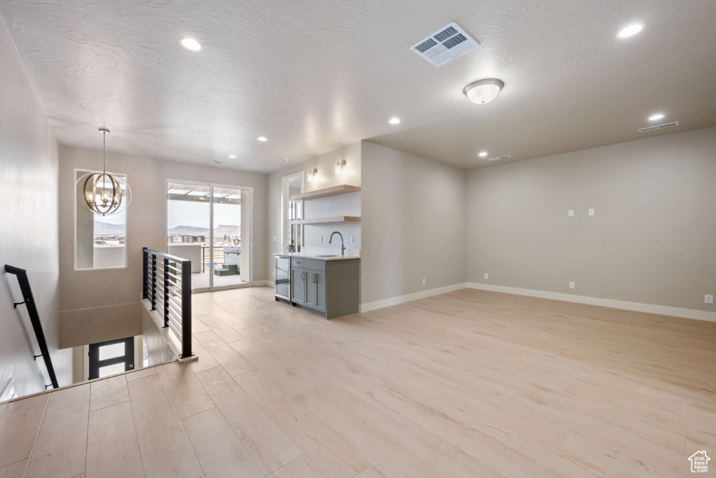 Unfurnished living room with a sink, light wood-type flooring, recessed lighting, baseboards, and a chandelier