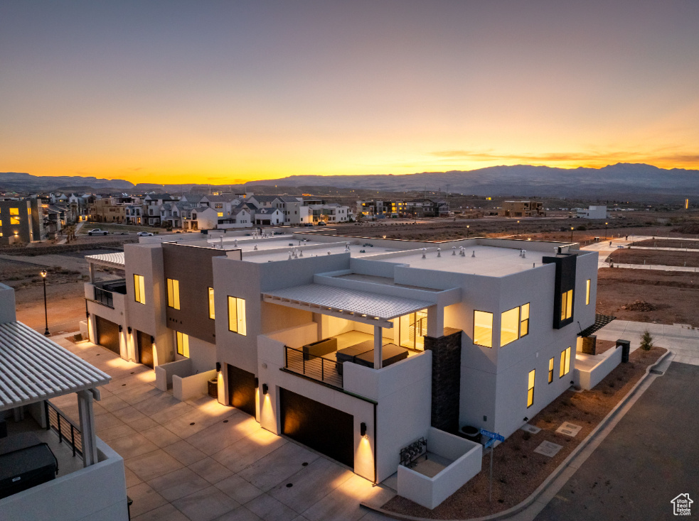 Back of house at dusk with stucco siding, a balcony, an attached garage, a mountain view, and driveway