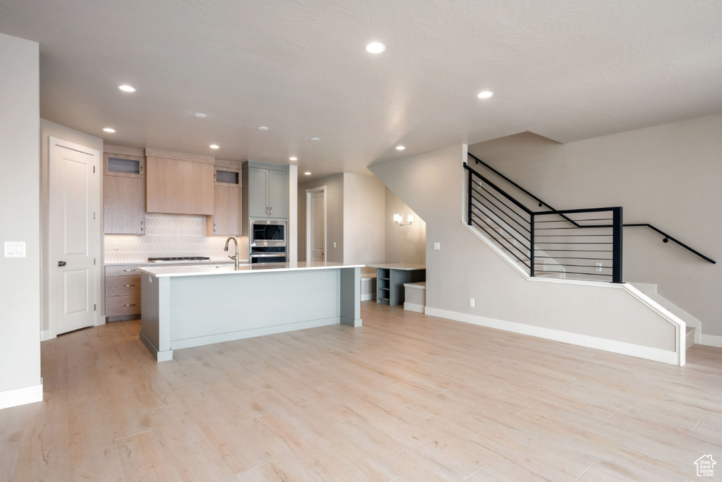 Kitchen featuring a kitchen island with sink, light countertops, backsplash, light wood-type flooring, and recessed lighting
