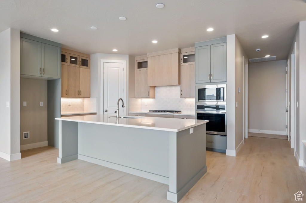 Kitchen with stainless steel appliances, a sink, backsplash, light countertops, and light wood-style flooring
