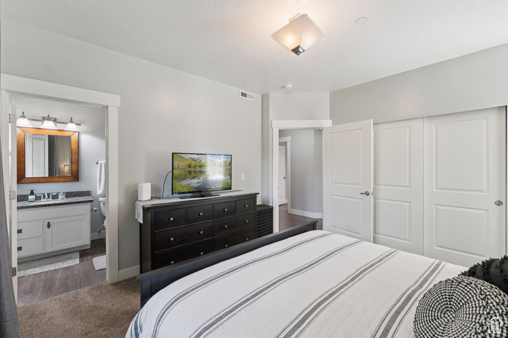 Carpeted bedroom featuring a closet, a sink, baseboards, and ensuite bath