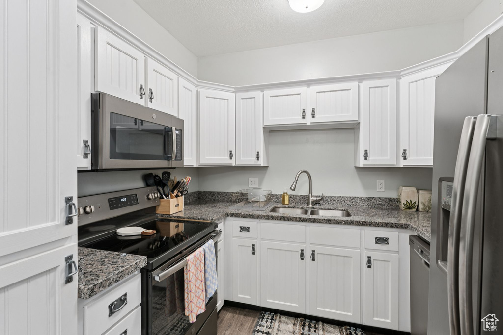 Kitchen featuring appliances with stainless steel finishes, a sink, white cabinetry, and dark stone counters