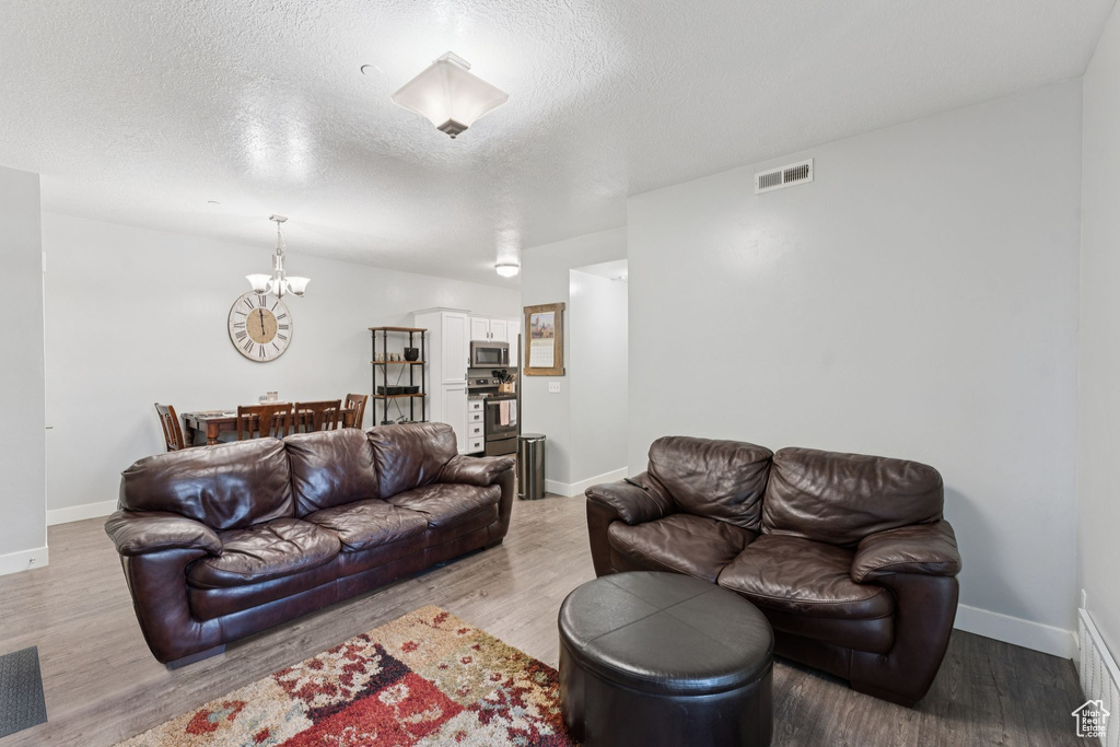 Living room featuring a chandelier, baseboards, wood finished floors, and a textured ceiling