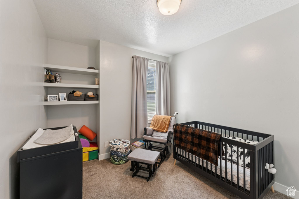 Bedroom with carpet, a nursery area, a textured ceiling, and baseboards