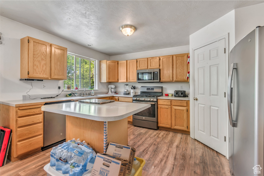 Kitchen with appliances with stainless steel finishes, light countertops, light wood-style floors, a kitchen island, and a sink