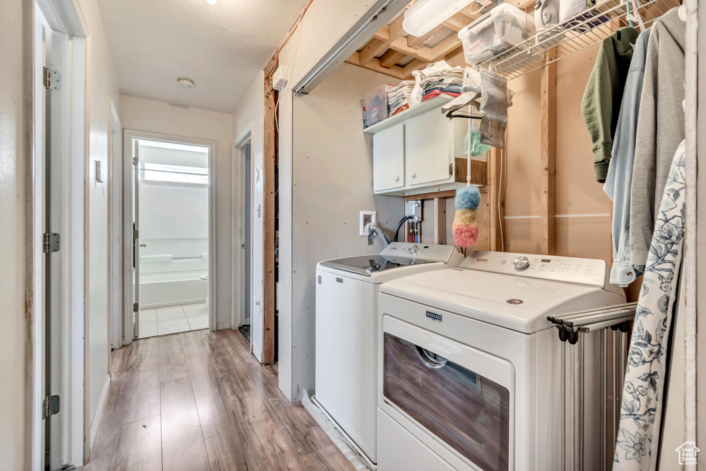 Washroom featuring washer and dryer, light wood-style floors, and cabinet space