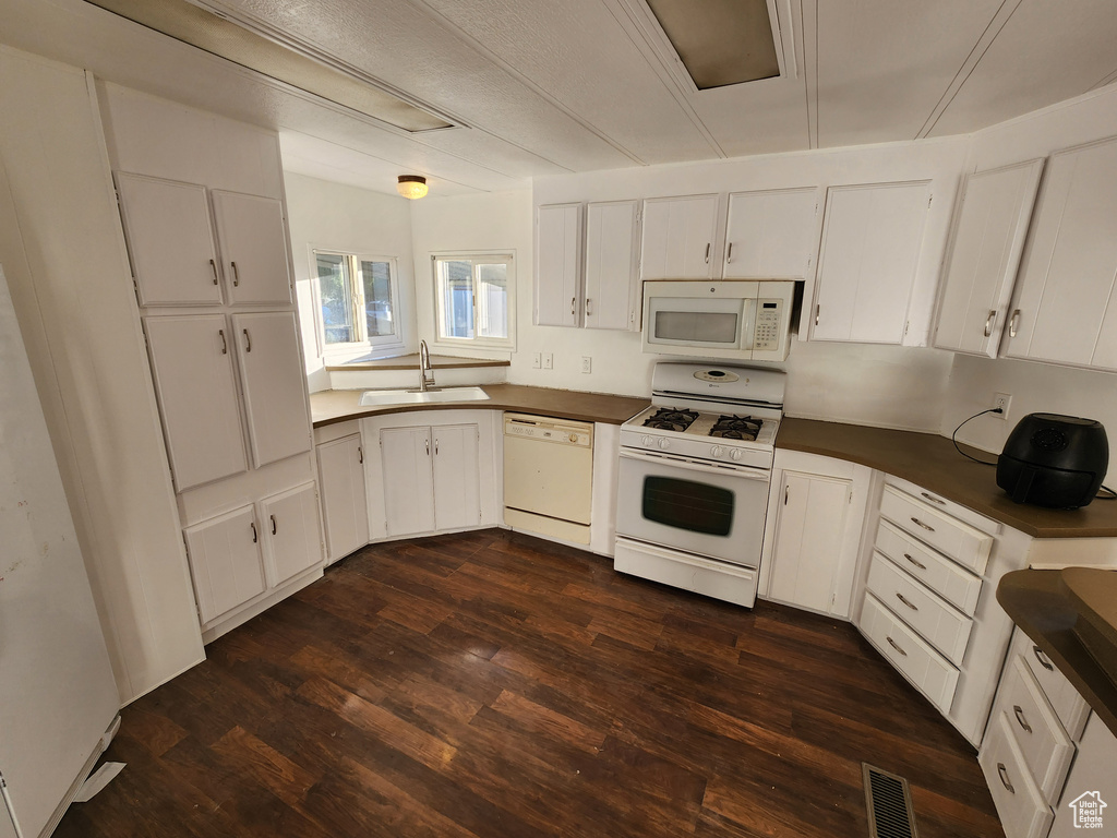 Kitchen featuring white appliances, a sink, dark countertops, dark wood-style flooring, and white cabinets
