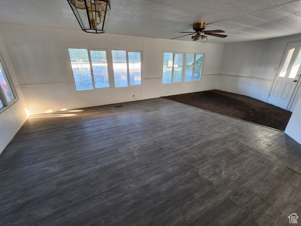 Empty room with plenty of natural light, a textured ceiling, dark wood-style flooring, and a ceiling fan