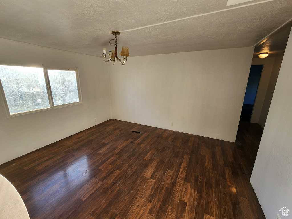 Empty room with a chandelier, dark wood finished floors, and a textured ceiling