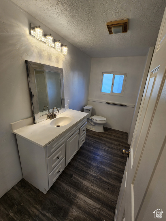 Half bathroom featuring wood finished floors, vanity, toilet, and a textured ceiling