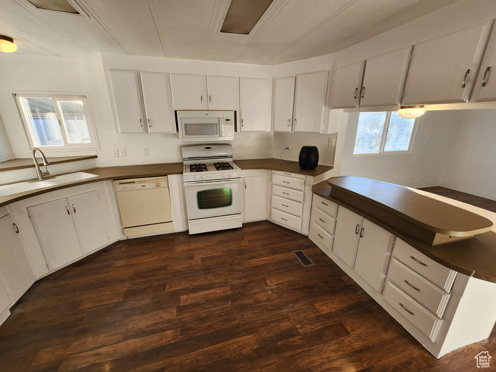 Kitchen with white appliances, a sink, dark countertops, dark wood-style floors, and white cabinets