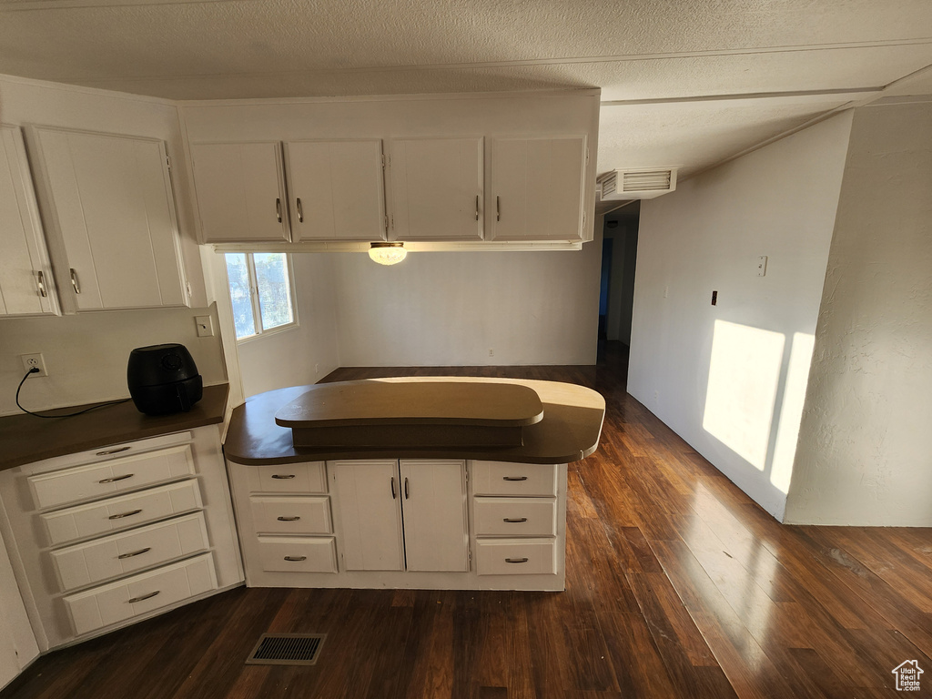 Kitchen with dark countertops, dark wood-style flooring, white cabinets, and a peninsula