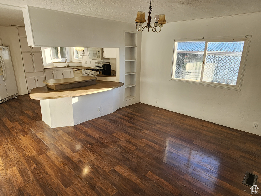 Kitchen with white appliances, a peninsula, dark wood finished floors, a chandelier, and a textured ceiling