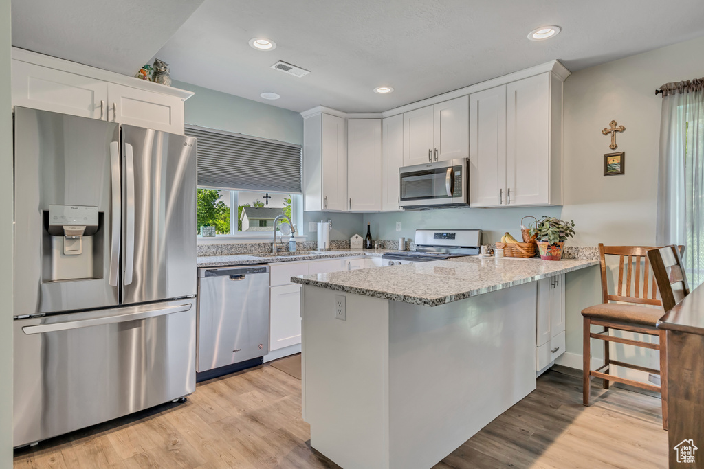 Kitchen featuring stainless steel appliances, a peninsula, white cabinets, light stone counters, and a sink