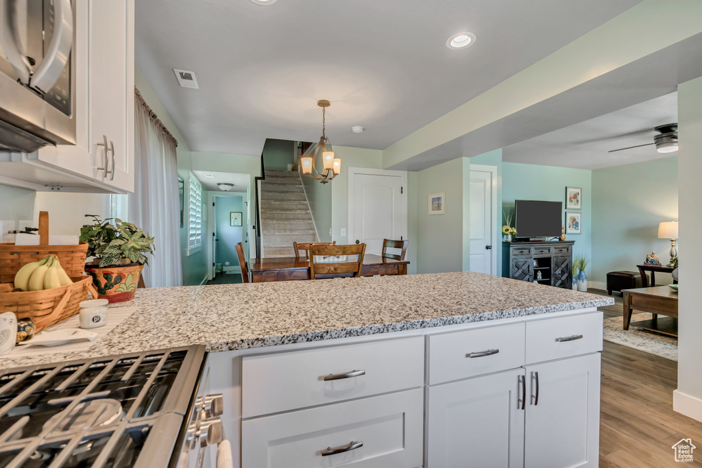Kitchen with stainless steel appliances, white cabinets, light stone countertops, light wood finished floors, and hanging light fixtures