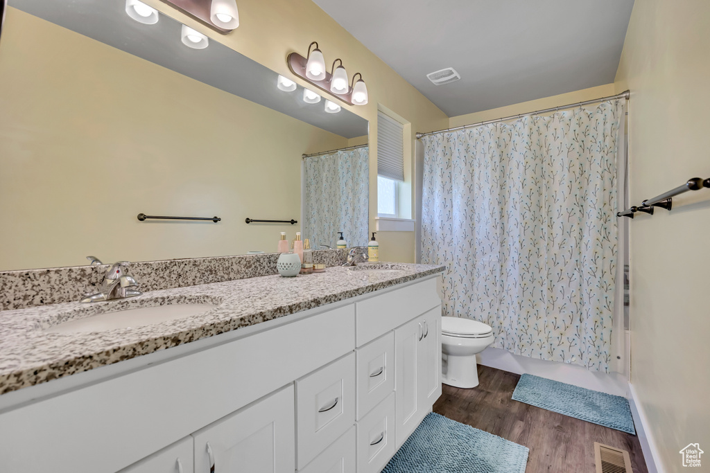 Bathroom with double vanity, toilet, and wood finished floors