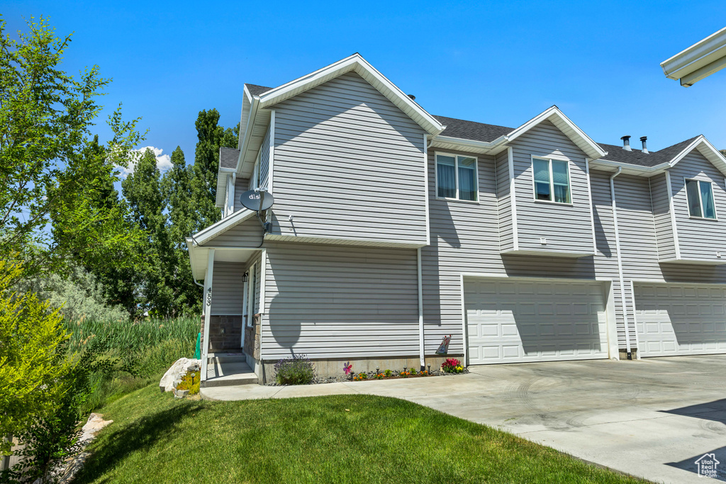 Back of house featuring concrete driveway, an attached garage, and a yard