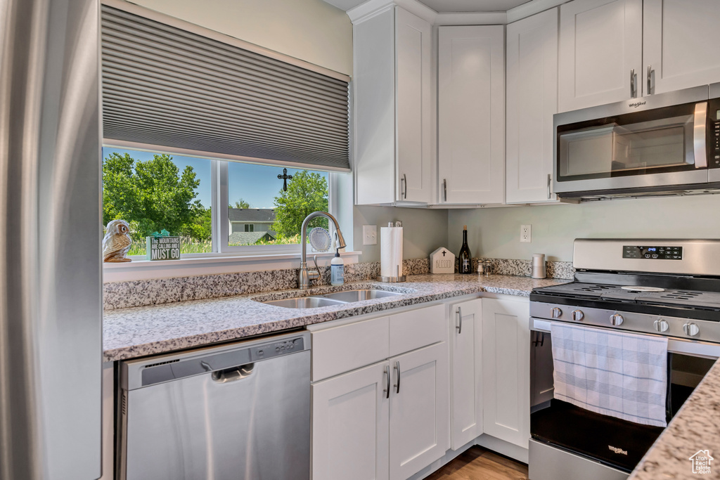 Kitchen featuring appliances with stainless steel finishes, a sink, white cabinetry, and light stone counters