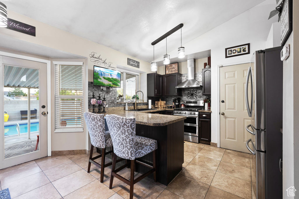 Kitchen featuring stainless steel appliances, wall chimney range hood, a peninsula, backsplash, and a sink