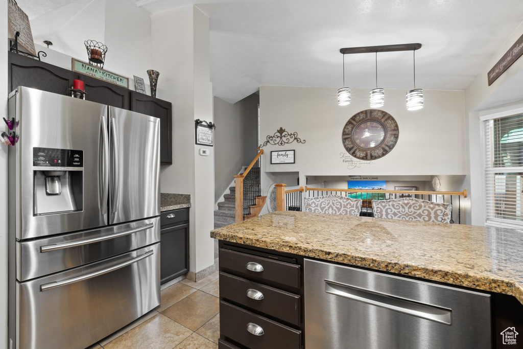 Kitchen with stainless steel appliances, light stone counters, light tile patterned floors, and pendant lighting