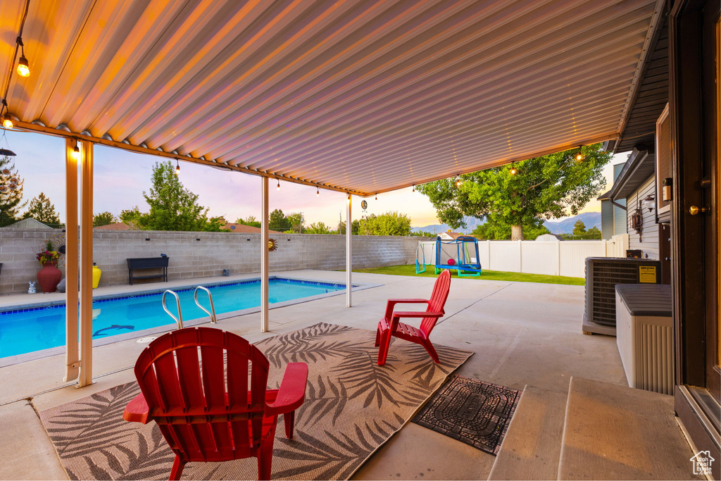 View of pool featuring a patio area, central AC, a fenced backyard, and a playground