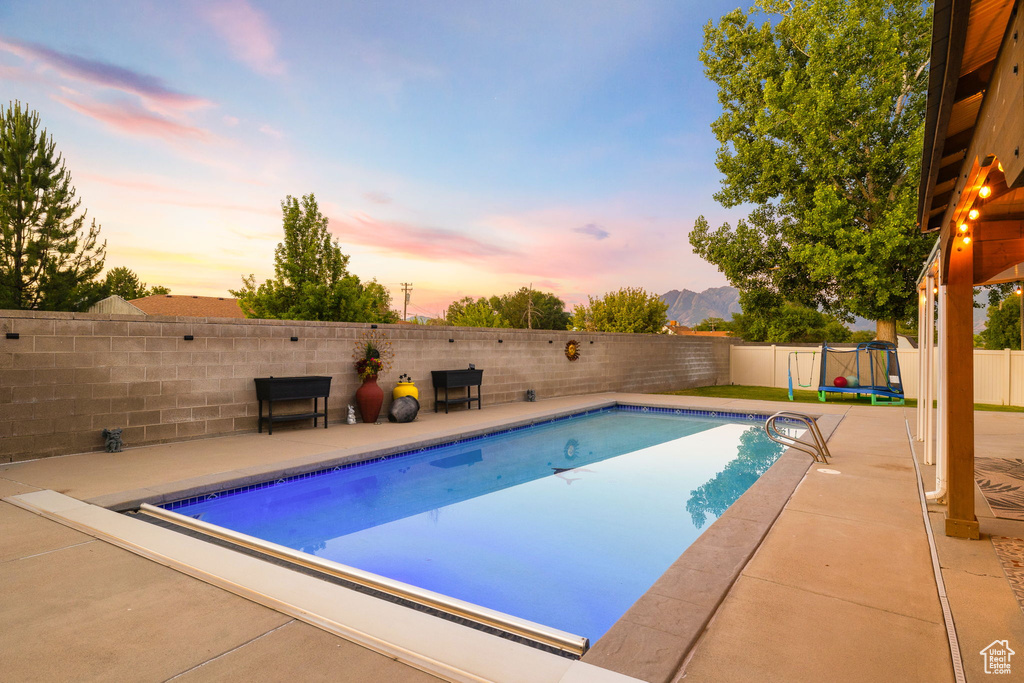 View of pool featuring a trampoline, a fenced backyard, a patio, and a mountain view