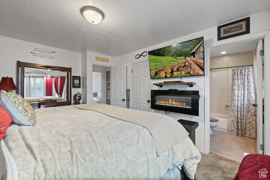 Carpeted bedroom featuring a glass covered fireplace, ensuite bathroom, and a textured ceiling