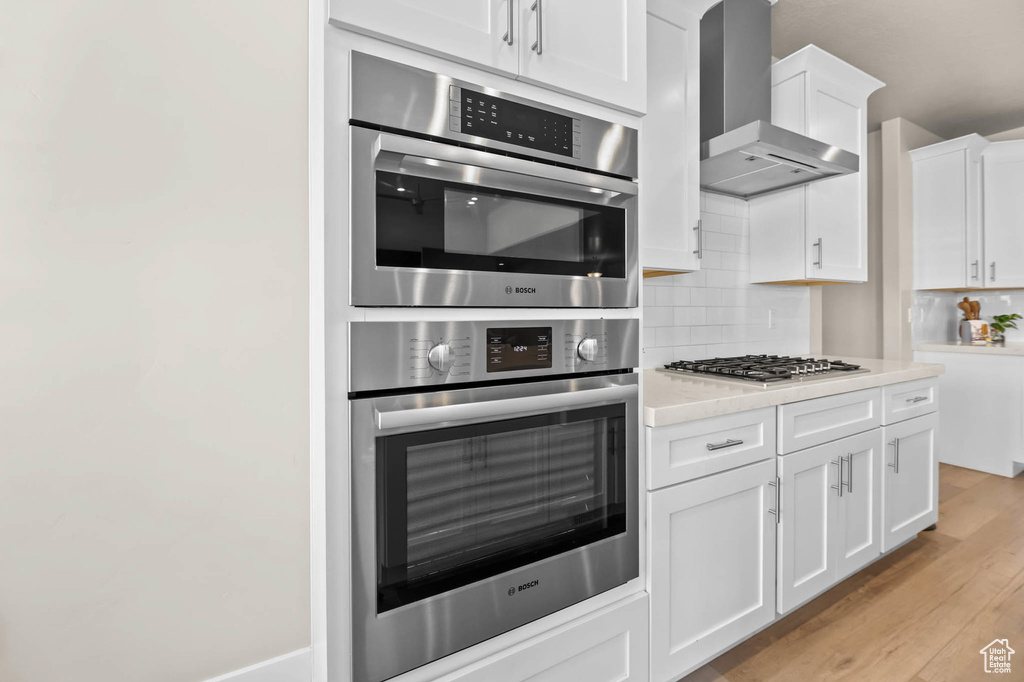 Kitchen featuring wall chimney exhaust hood, light countertops, backsplash, and light wood-style flooring