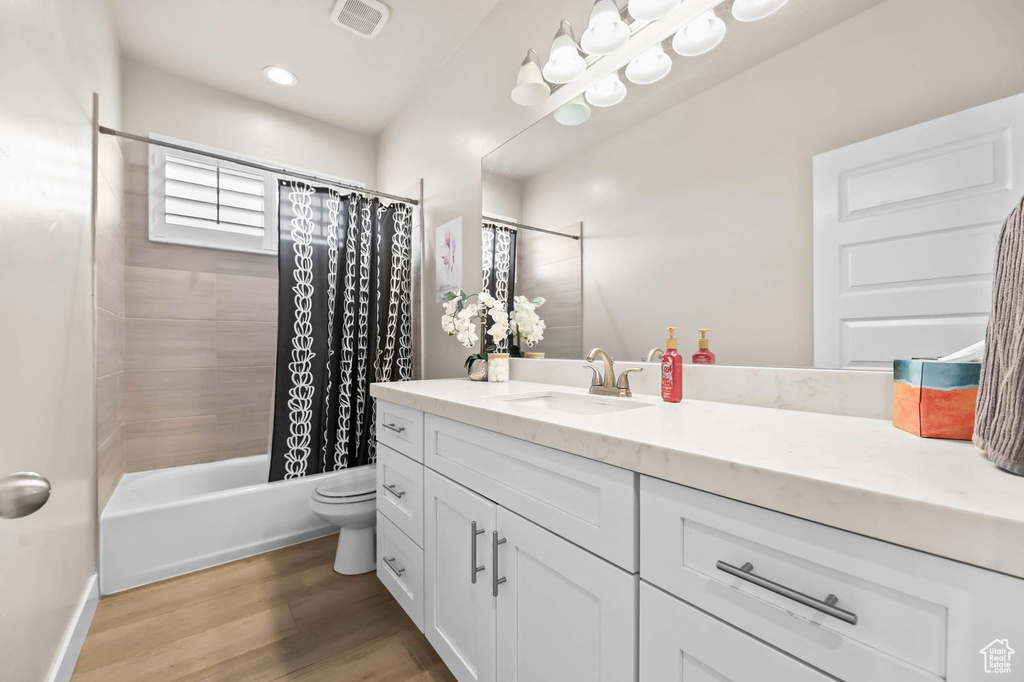 Full bath featuring vanity, shower / bath combo with shower curtain, wood finished floors, and toilet
