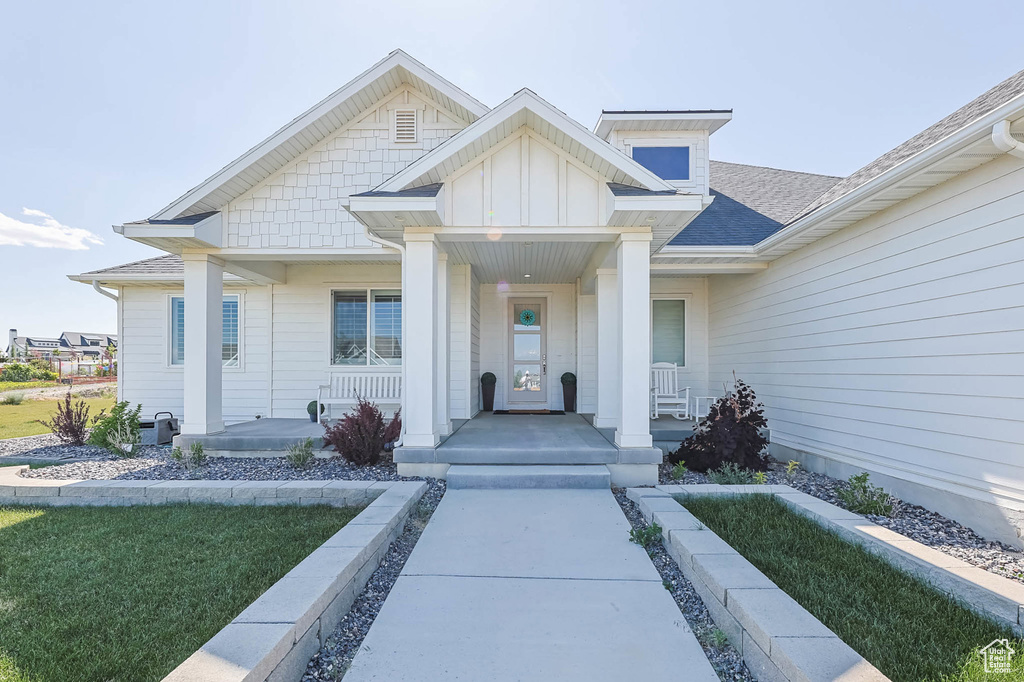 Entrance to property featuring covered porch, a shingled roof, and board and batten siding