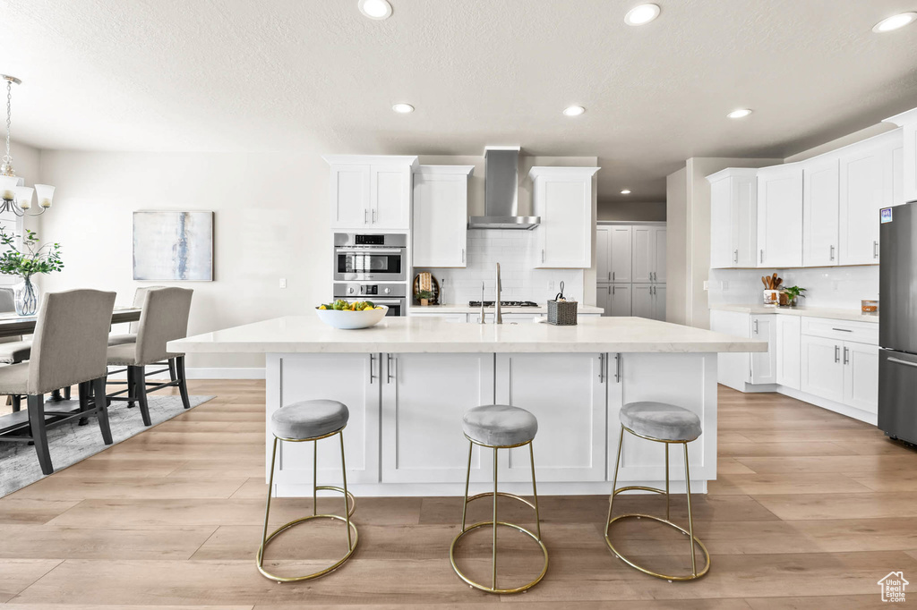 Kitchen with wall chimney exhaust hood, stainless steel appliances, recessed lighting, light wood finished floors, and tasteful backsplash