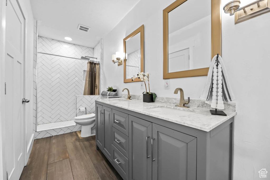 Full bathroom with toilet, double vanity, a tile shower, wood finished floors, and recessed lighting