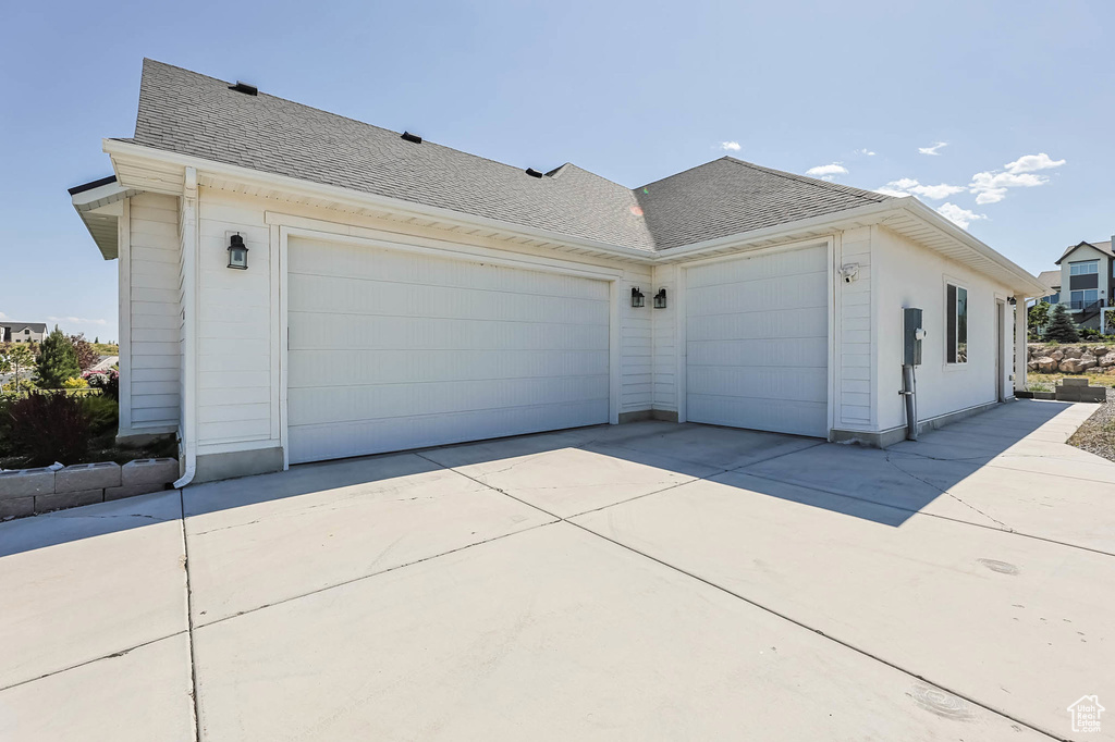 View of side of home featuring a shingled roof, driveway, and a garage