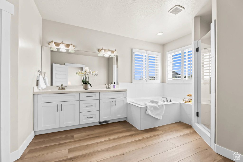 Full bathroom featuring double vanity, a garden tub, wood finished floors, a shower stall, and a textured ceiling