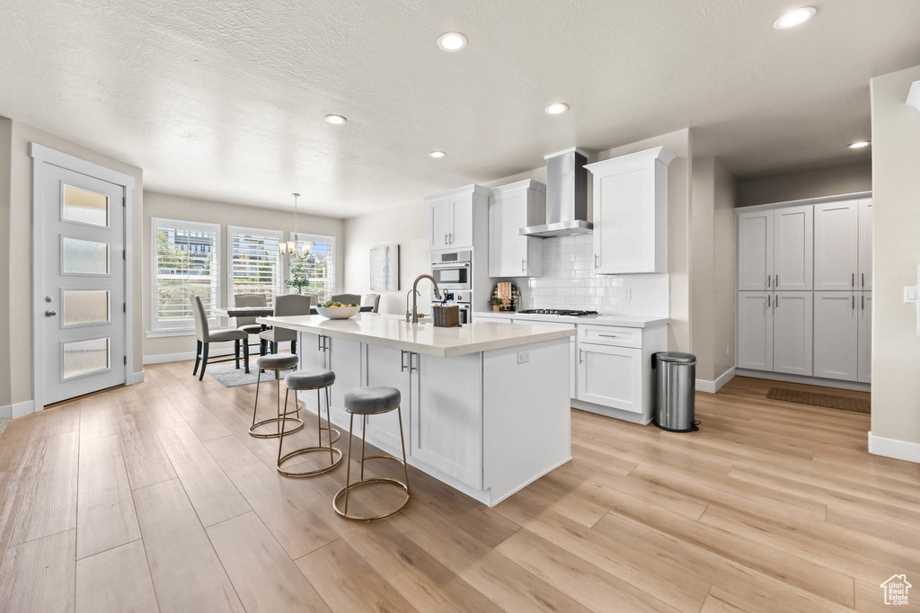 Kitchen featuring wall chimney range hood, baseboards, a breakfast bar area, light wood-style flooring, and recessed lighting