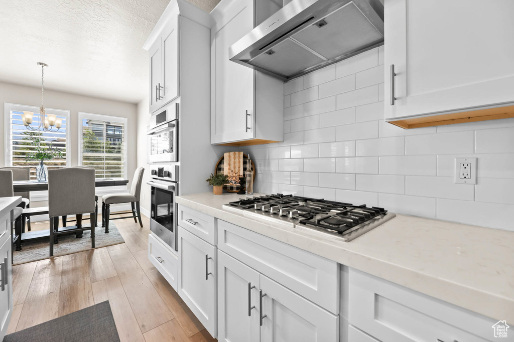 Kitchen with range hood, appliances with stainless steel finishes, light countertops, white cabinets, and a chandelier