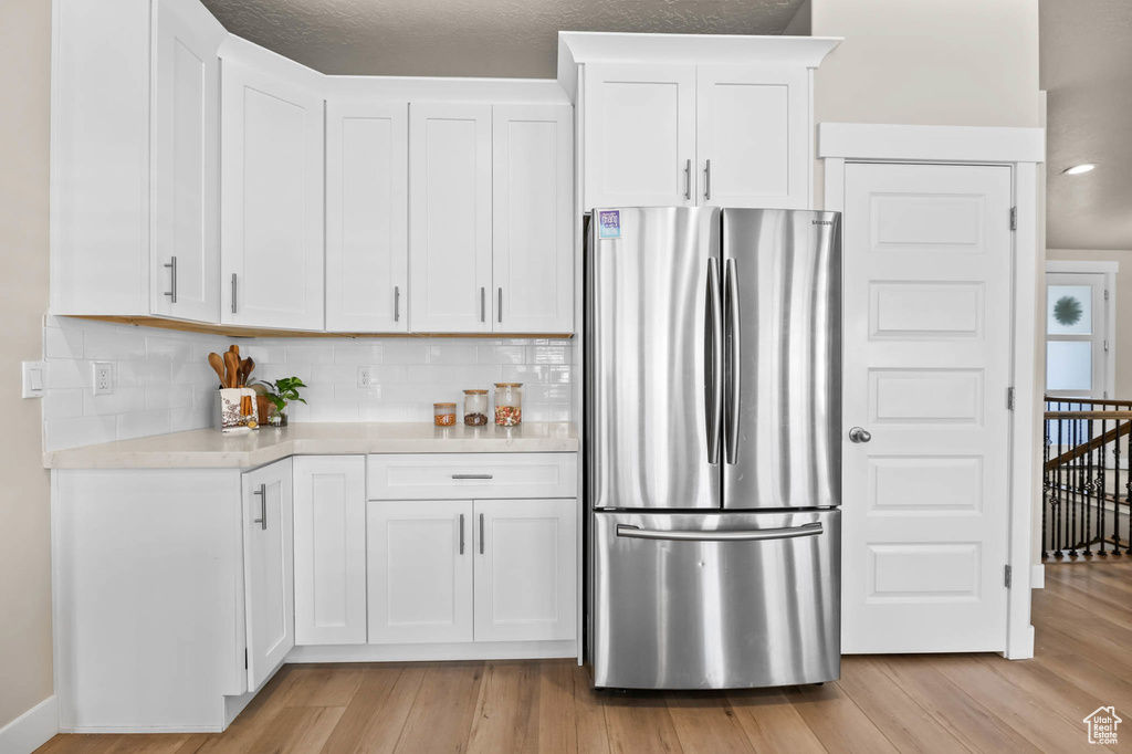 Kitchen featuring freestanding refrigerator, light countertops, light wood-style floors, and backsplash