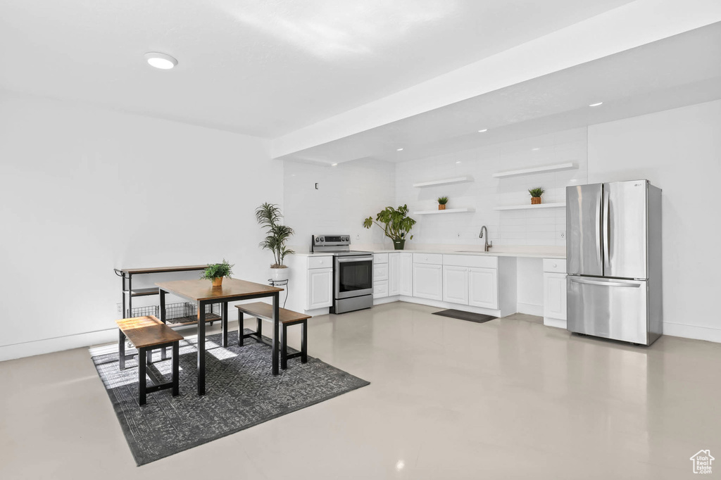 Kitchen with stainless steel appliances, open shelves, white cabinetry, light countertops, and a sink