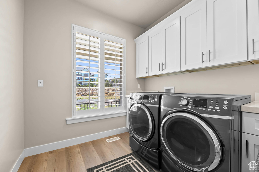Washroom with cabinet space, washing machine and clothes dryer, baseboards, and light wood-style flooring