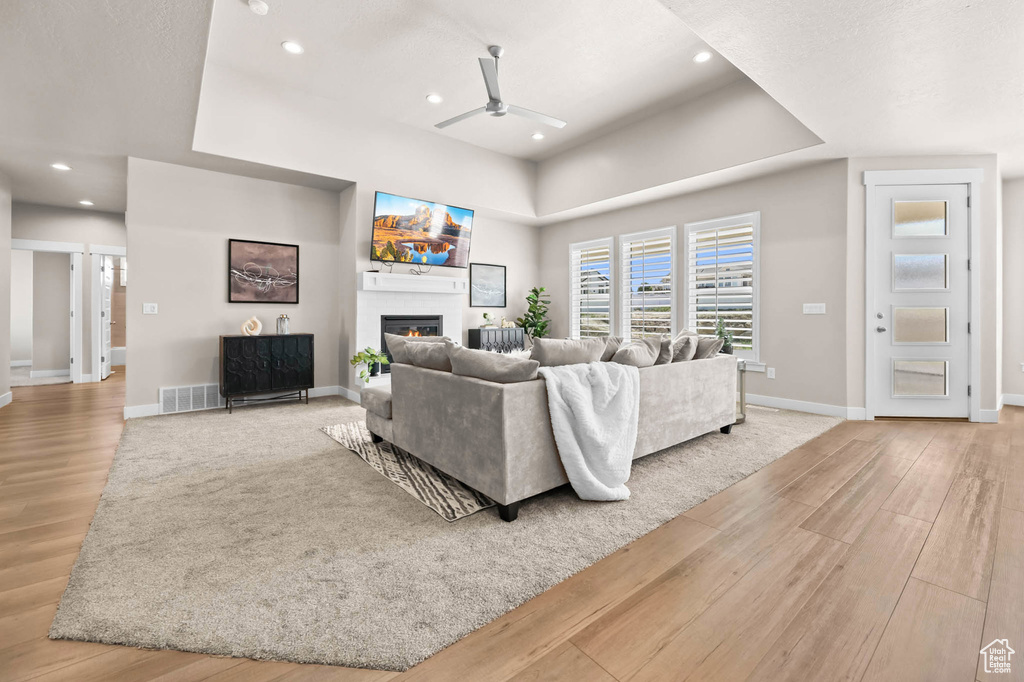 Living area with a ceiling fan, wood finished floors, a glass covered fireplace, a raised ceiling, and baseboards