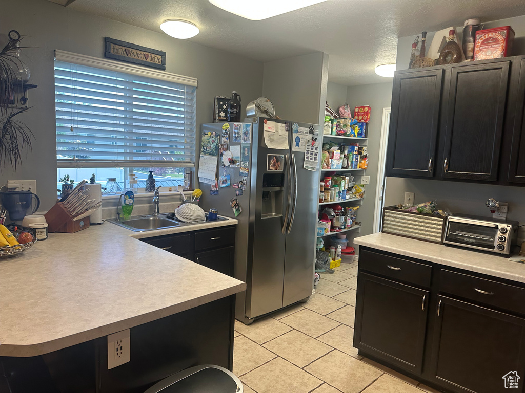 Kitchen featuring stainless steel fridge with ice dispenser, light tile patterned floors, light countertops, dark cabinets, and a sink